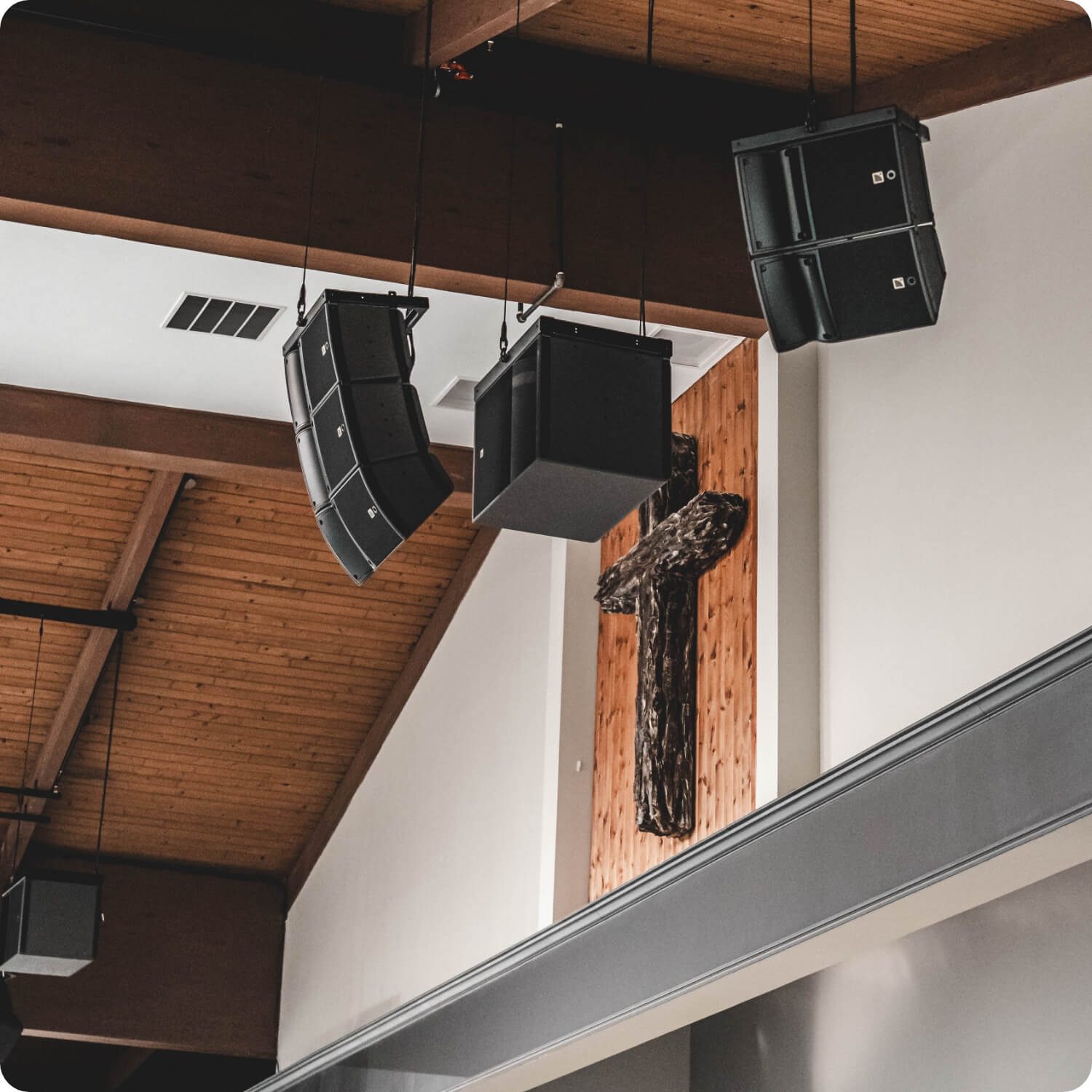 Line-array speakers hung beside a wooden cross under the chapel's timber ceiling.