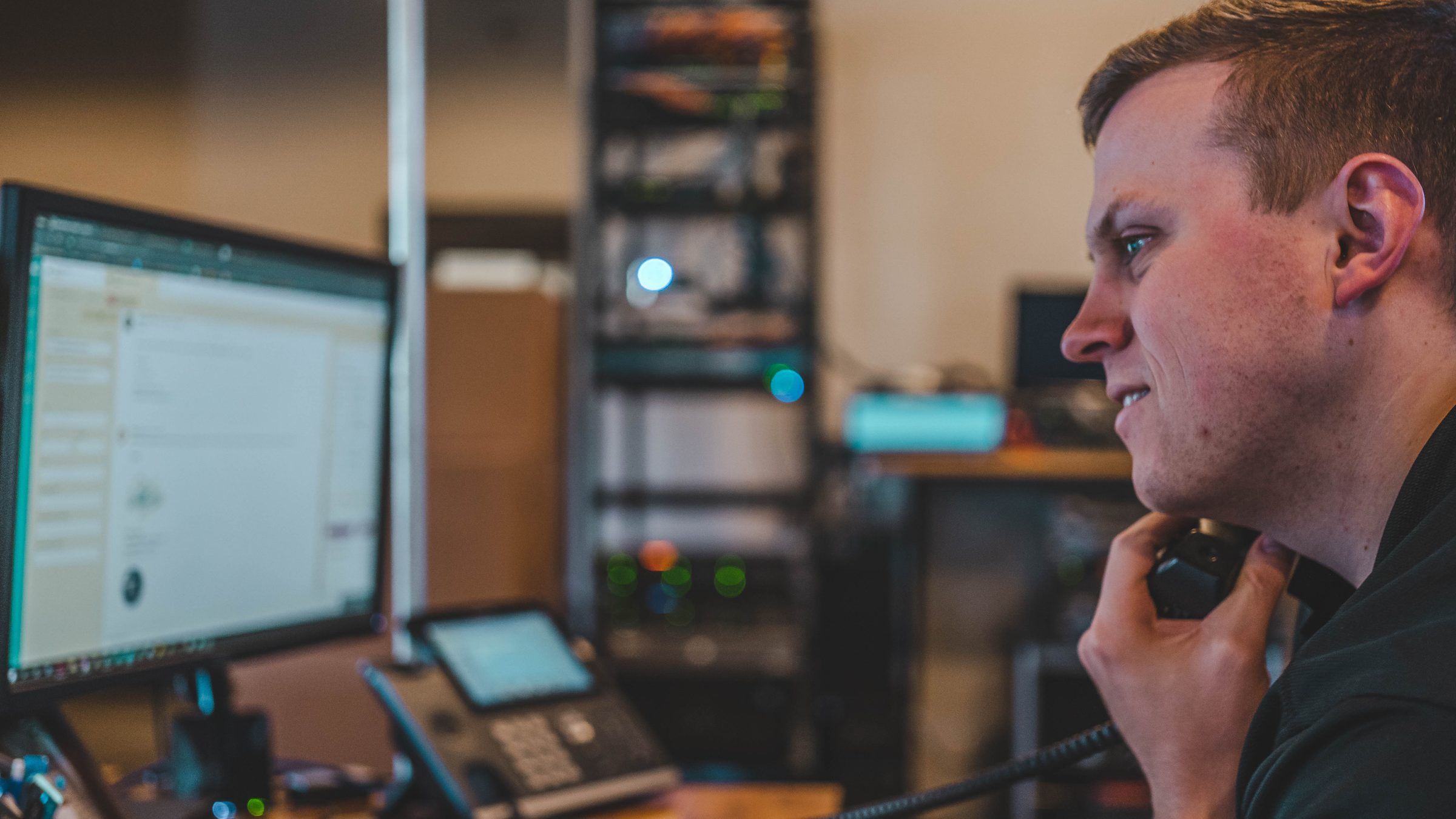 David on a support call, with a server rack lit up behind the desk.